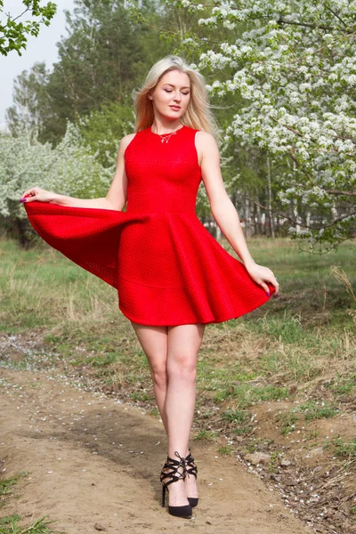 Meisje in een rode korte jurk tegen de achtergrond van een bloeiende appelboomgaard — Stockfoto