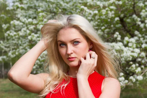 Girl in a red short dress against the background of a blooming apple orchard — Stock Photo, Image