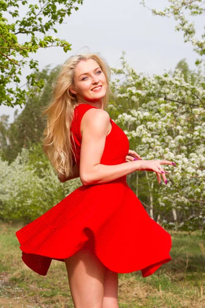 Meisje in een rode korte jurk tegen de achtergrond van een bloeiende appelboomgaard — Stockfoto