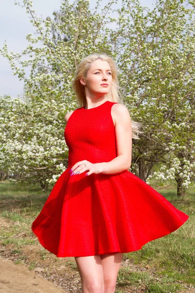 Flicka i en röd kort klänning mot bakgrund av en blommande äppelträdgård — Stockfoto