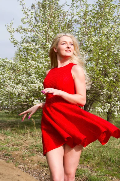 Flicka i en röd kort klänning mot bakgrund av en blommande äppelträdgård — Stockfoto