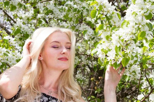花盛りの木の背景に庭で若い金髪 — ストック写真