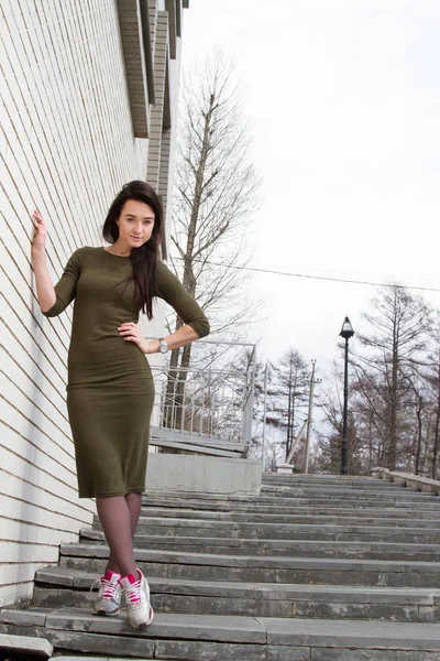 Meisje in een jurk en sneakers staat in de buurt van een muur — Stockfoto
