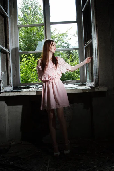 Mädchen in kurzem rosa Kleid steht vor einem Fenster in einem verlassenen Haus — Stockfoto