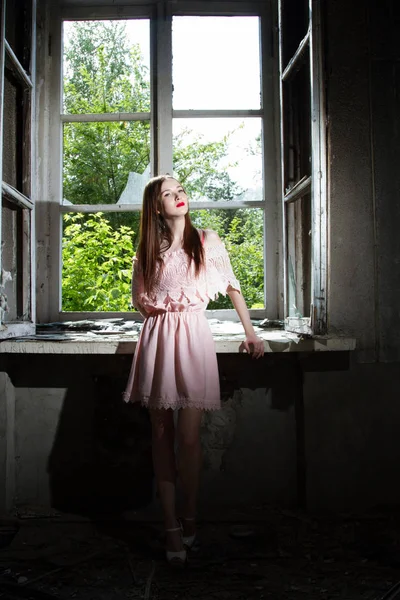 Mädchen in kurzem rosa Kleid steht vor einem Fenster in einem verlassenen Haus — Stockfoto