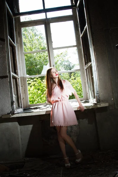 Mädchen in kurzem rosa Kleid steht vor einem Fenster in einem verlassenen Haus — Stockfoto