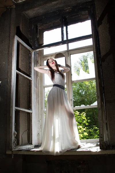 Schlankes junges Mädchen in weißem Kleid auf Fensterbank in verlassenem Haus — Stockfoto
