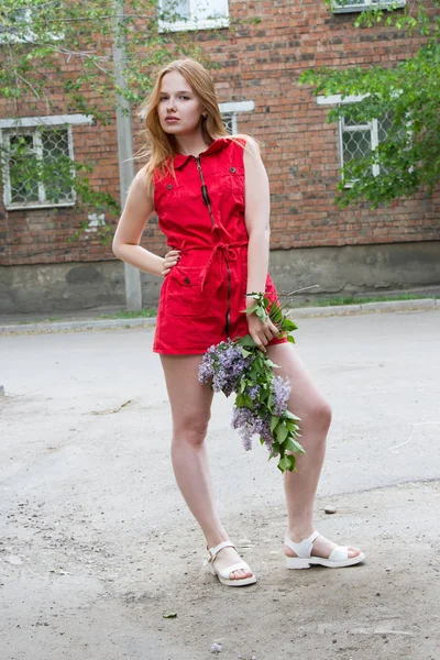 Mädchen in einem kurzen roten Kleid mit einem Strauß Flieder — Stockfoto