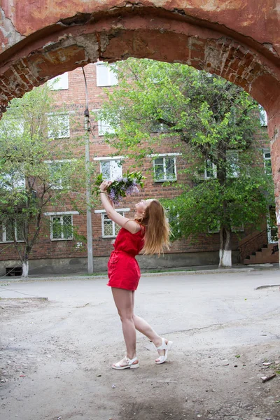 Mädchen in einem kurzen roten Kleid mit einem Strauß Flieder — Stockfoto