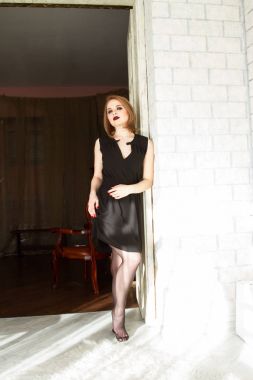 Sarışın siyah kısa bir elbise içinde kapısında duruyor