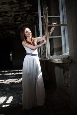 Beyaz bir elbise içinde gelin yanmış bir ev pencere tarafından duruyor