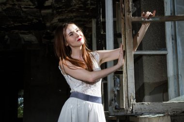 Beyaz bir elbise içinde gelin yanmış bir ev pencere tarafından duruyor