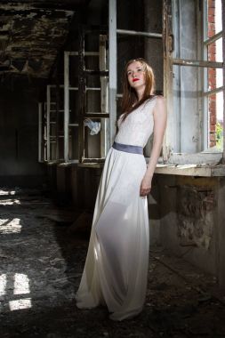 Beyaz bir elbise içinde gelin yanmış bir ev pencere tarafından duruyor