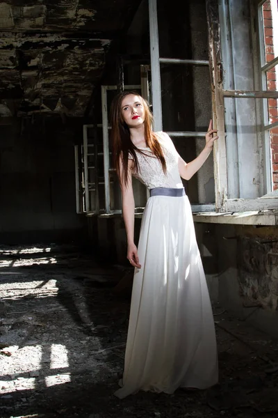 Braut in weißem Kleid steht am Fenster eines abgebrannten Hauses — Stockfoto