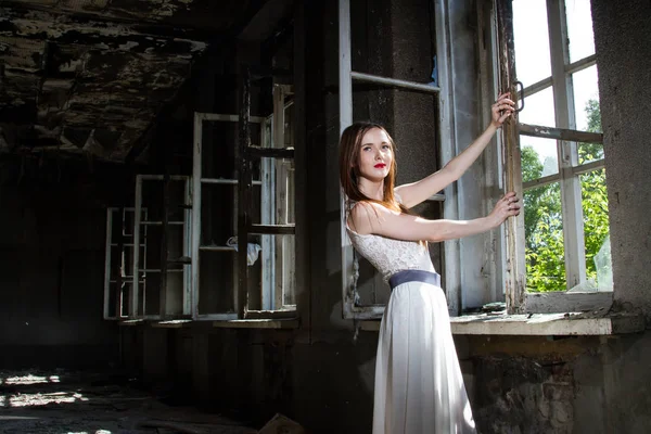 Braut in weißem Kleid steht am Fenster eines abgebrannten Hauses — Stockfoto