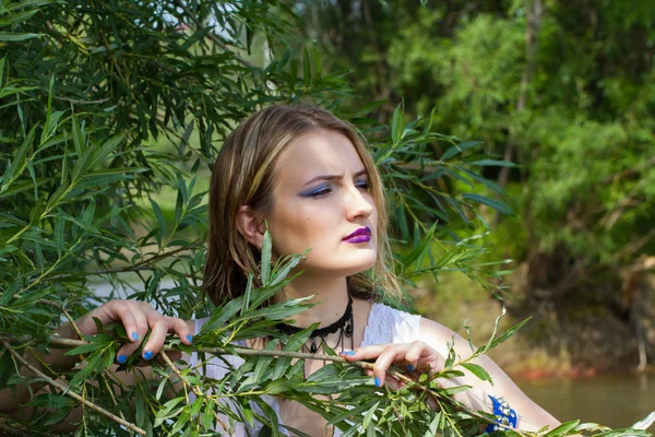 Девушка с ярким макияжем смотрит из-за ветвей — стоковое фото