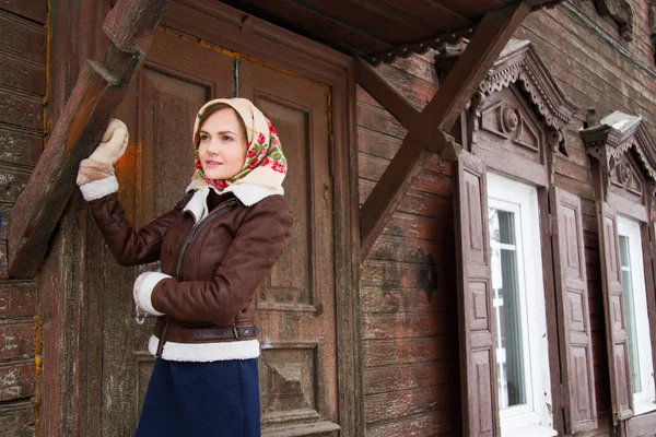 Κορίτσι σε ένα πολύχρωμο μαντήλι στέκεται στη βεράντα του ένα παλιό ξύλινο σπίτι — Φωτογραφία Αρχείου