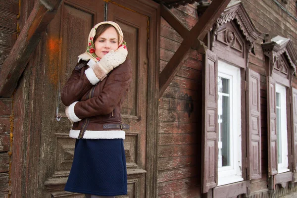 Ragazza in una sciarpa colorata è in piedi sul portico di una vecchia casa di legno — Foto Stock