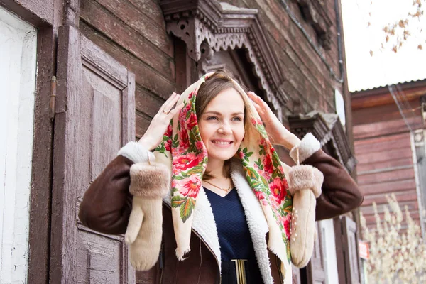 Ragazza in una sciarpa colorata è in piedi sul portico di una vecchia casa di legno — Foto Stock