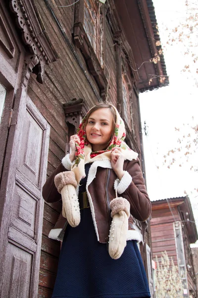 Ragazza in una sciarpa colorata è in piedi sul portico di una vecchia casa di legno — Foto Stock