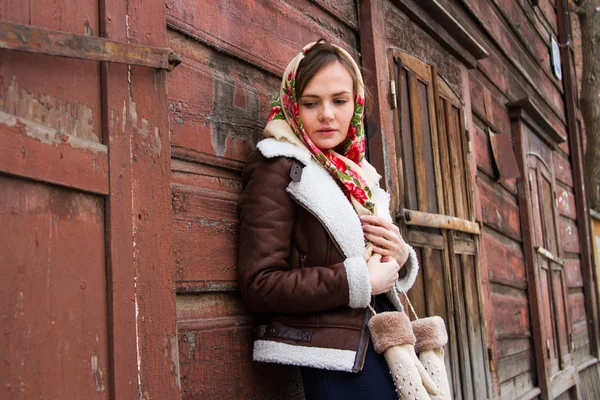 Girl in a colorful scarf is standing on the porch of an old wooden house — Stock Photo, Image