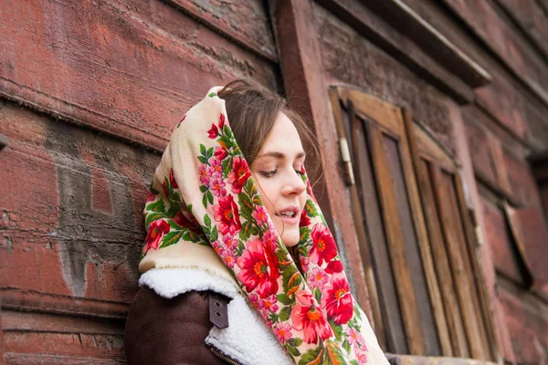 Girl in a colorful scarf is standing on the porch of an old wooden house — Stock Photo, Image