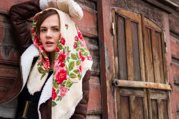 Girl in a colorful scarf is standing on the porch of an old wooden house — Stock Photo, Image