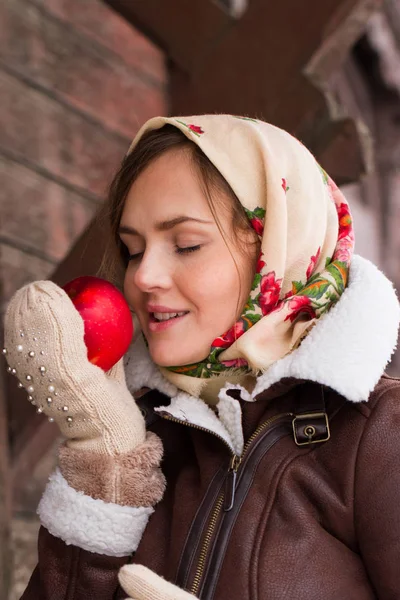 Chica en una bufanda de colores y con una manzana roja está de pie en el porche de una antigua casa de madera —  Fotos de Stock