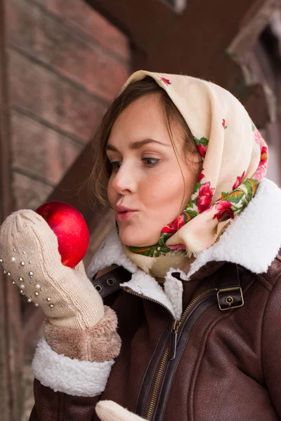 Девушка в красочном шарфе и с красным яблоком стоит на крыльце старого деревянного дома — стоковое фото