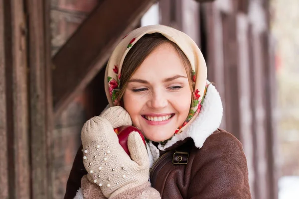 Girl in a colorful scarf and with a red apple is standing on the porch of an old wooden house — Stock Photo, Image