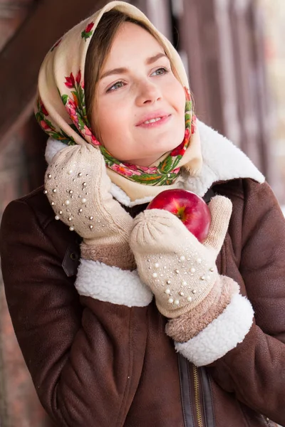 Chica en una bufanda de colores y con una manzana roja está de pie en el porche de una antigua casa de madera —  Fotos de Stock