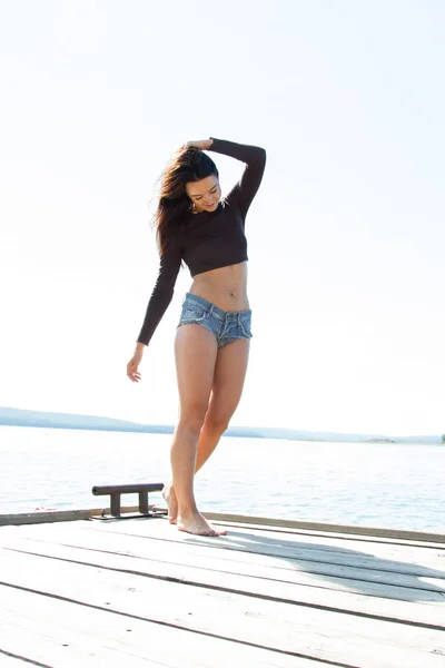 Schlankes Mädchen in kurzen Shorts steht auf der Seebrücke — Stockfoto