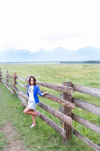 Молодая девушка в синей куртке стоит у длинного деревянного забора — стоковое фото