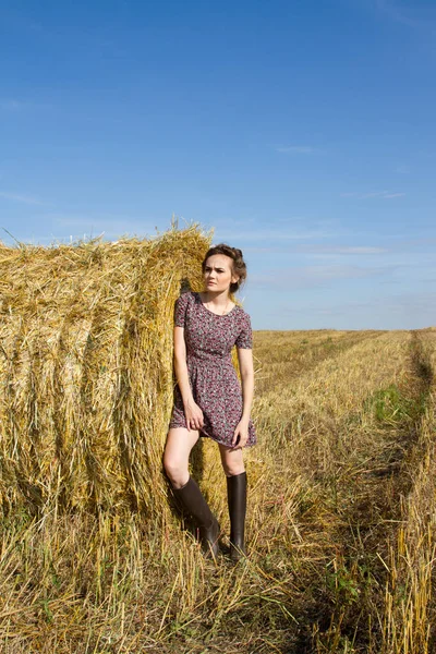 Mädchen in Gummistiefeln und kurzem Rock steht neben Strohballen — Stockfoto