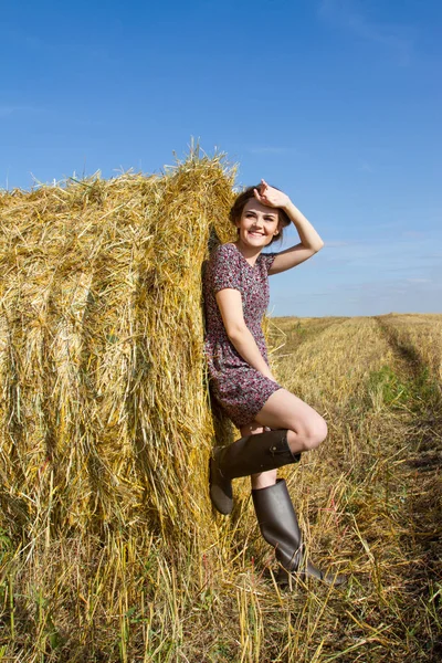 Ragazza in stivali di gomma e una gonna corta è in piedi vicino a una balla di paglia — Foto Stock