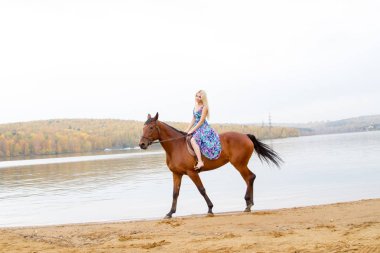 Bir göl kıyısında bir atlı bir akşam elbiseli bir kız atlar