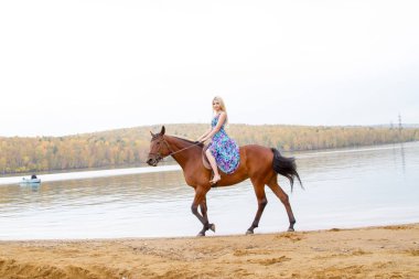 Bir göl kıyısında bir atlı bir akşam elbiseli bir kız atlar