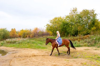 Bir göl kıyısında bir atlı bir akşam elbiseli bir kız atlar