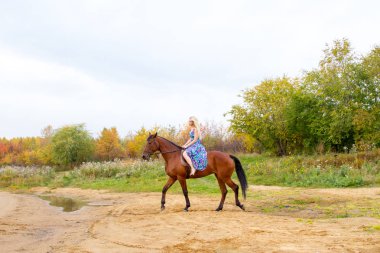Bir göl kıyısında bir atlı bir akşam elbiseli bir kız atlar
