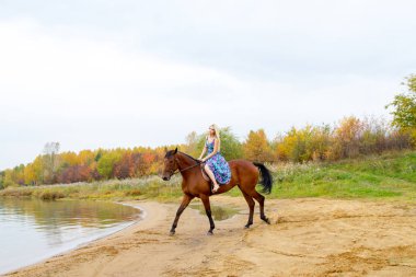 Bir göl kıyısında bir atlı bir akşam elbiseli bir kız atlar