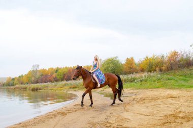 Bir göl kıyısında bir atlı bir akşam elbiseli bir kız atlar