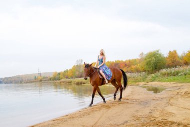 Bir göl kıyısında bir atlı bir akşam elbiseli bir kız atlar