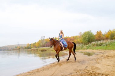 Bir göl kıyısında bir atlı bir akşam elbiseli bir kız atlar