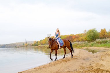 Bir göl kıyısında bir atlı bir akşam elbiseli bir kız atlar
