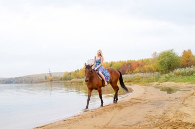 Bir göl kıyısında bir atlı bir akşam elbiseli bir kız atlar