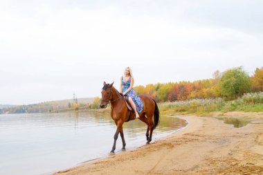 Bir göl kıyısında bir atlı bir akşam elbiseli bir kız atlar