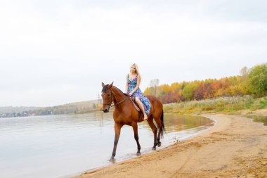 Bir göl kıyısında bir atlı bir akşam elbiseli bir kız atlar
