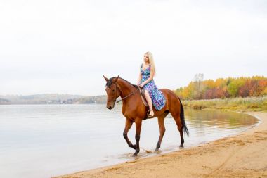 Bir göl kıyısında bir atlı bir akşam elbiseli bir kız atlar