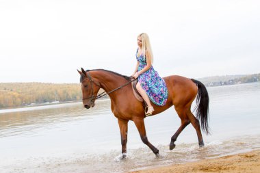 Bir göl kıyısında bir atlı bir akşam elbiseli bir kız atlar