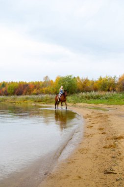 Bir göl kıyısında bir atlı bir akşam elbiseli bir kız atlar